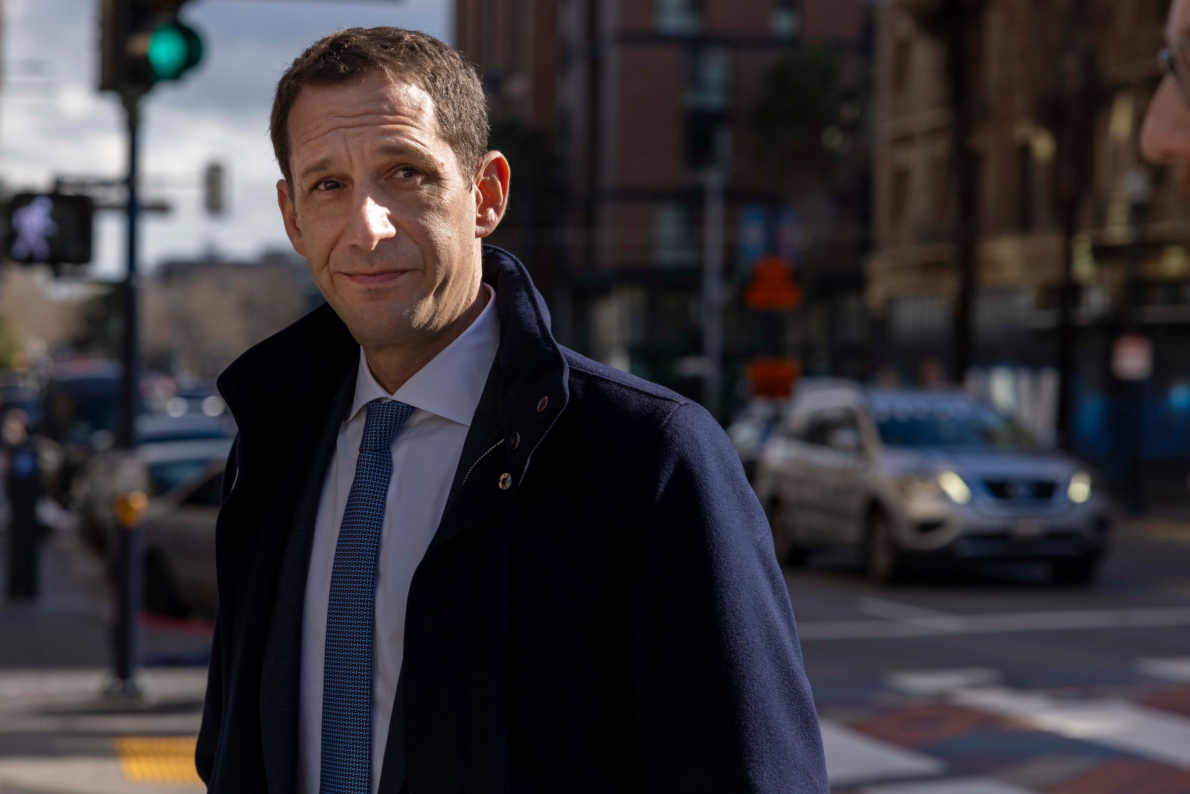 Mayor Daniel Lurie in a coat standing at an intersection.